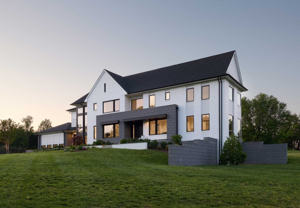 An exterior photo of a modern transitional home in white brick with a grey block geometric shape at the front entrance, complemented by grey block foundation and retaining walls.