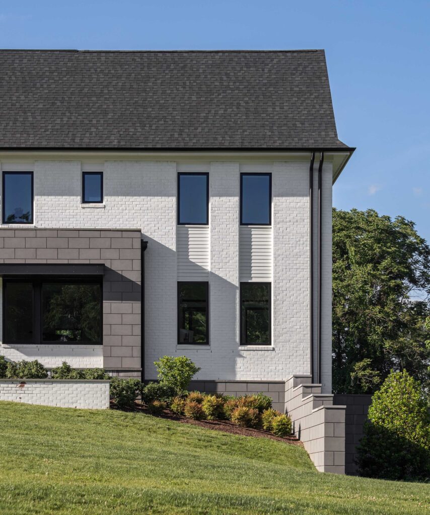 An exterior detail showing 2 pairs of dark symmetrical windows with white paneling in between on white brick. Grey block visible to the left and foundation.