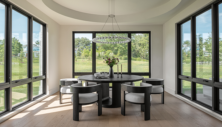 A morning room of white walls and black windows with a circular tray ceiling and round chandelier. A black table and chairs in the center.