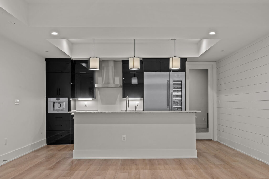 A wet bar painted white with black cabinetry behind, a modern fridge and wine fridge, fumehood are visible, a glass door to the right