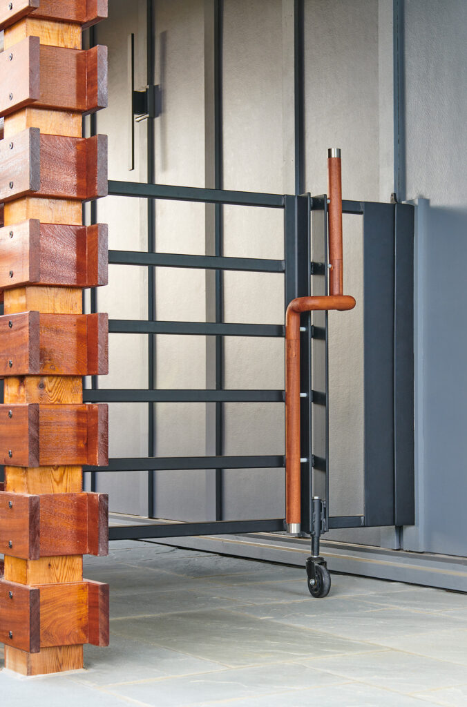 A contemporary gate of grey iron with a stained wood handle capped with chrome.