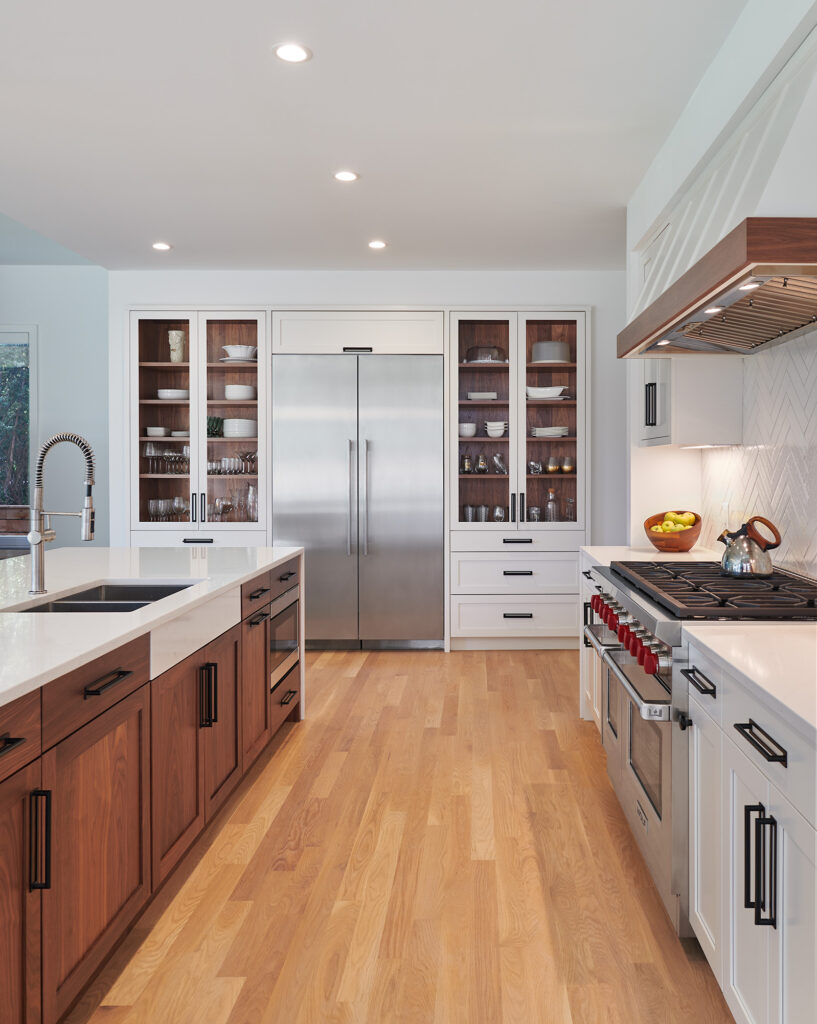 A modern kitchen with counter depth oversized refrigerator, professional range, stained wood lined cabinets with glass doors
