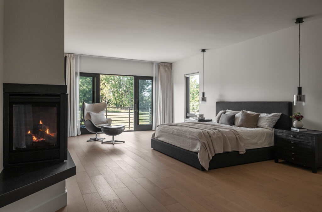 An Owner's Suite bedroom with double sided fireplace in the foreground and balcony with horizontal rails on the far wall.