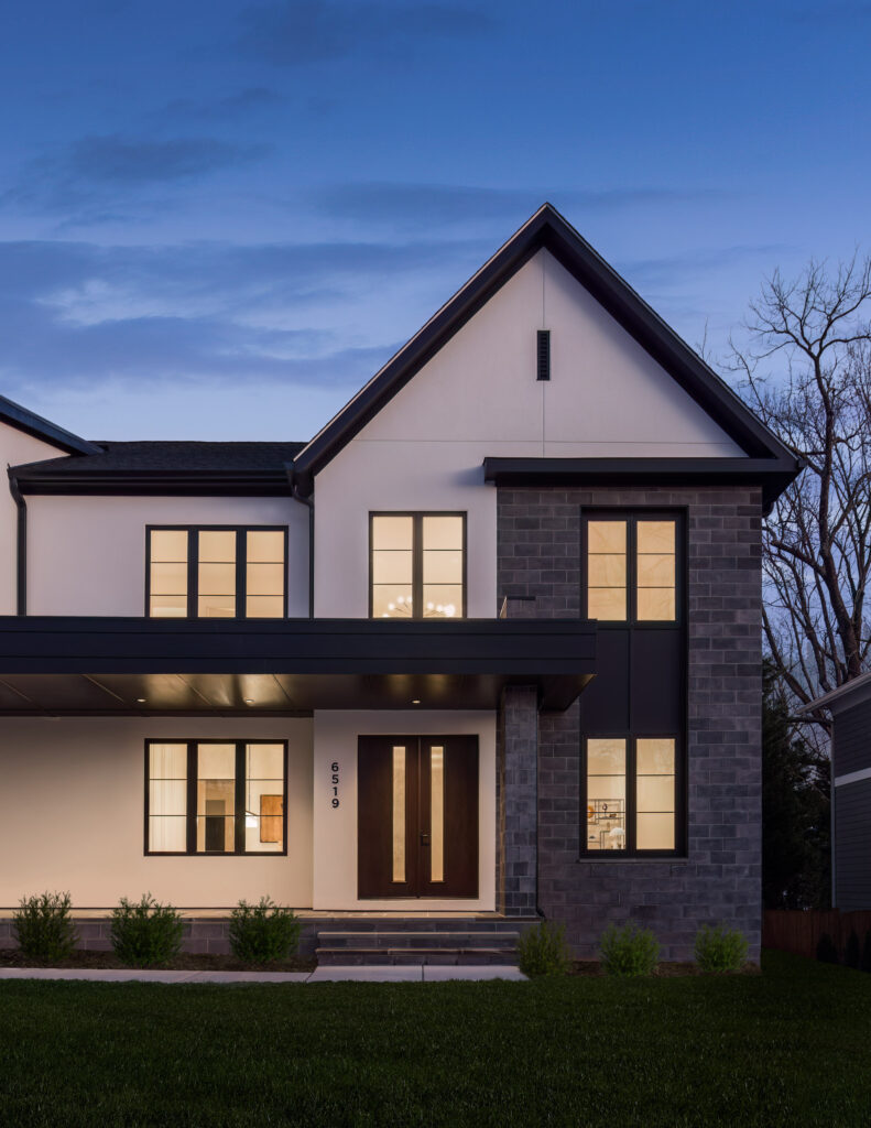 A photo of one side of a transitional modern home of stucco and geometric shapes of grey architectural block, with dark accents and wood stain front and garage door