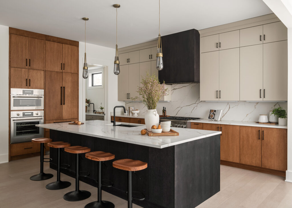 A modern kitchen with a mix of white, dark and light stained cabinetry, quartz counter and island tops, in the far corner a butler's pantry is visible.