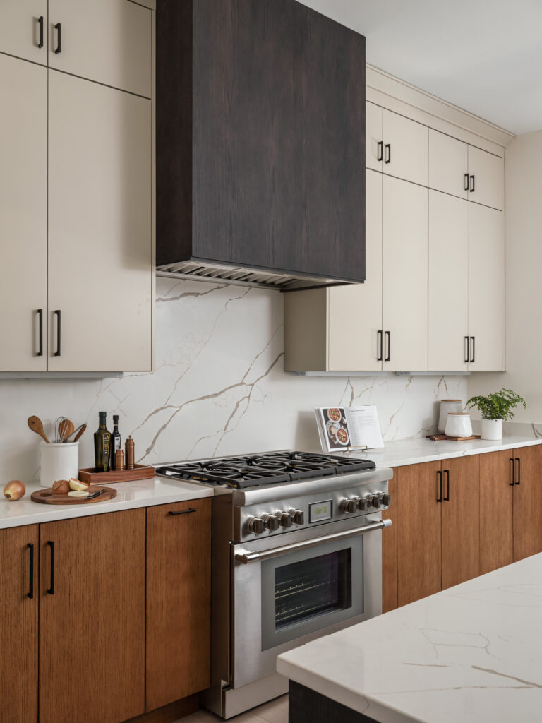 A detail photo showing a professional range, fume hood with stained wood cover, white painted cabinets above, stained below.