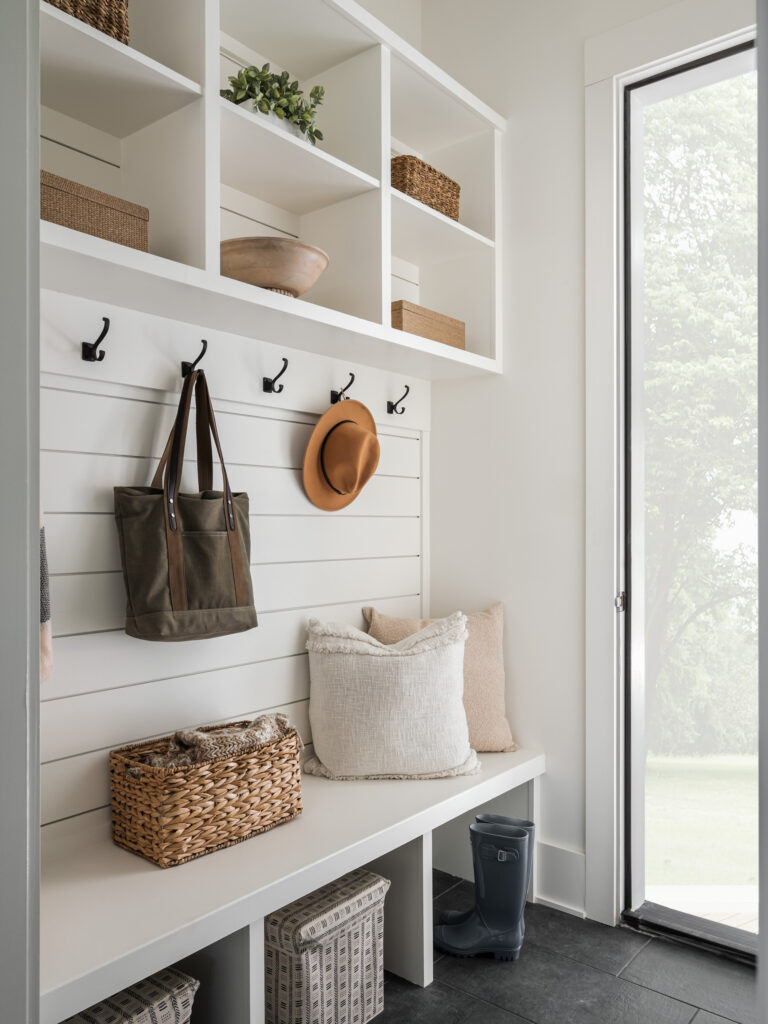 A mudroom with white shiplap siding, bench with cubbies and built in shelving above.