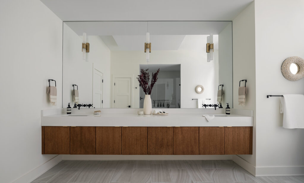 A floating vanity of stained wood doors, white top, contemporary white and brass lighting