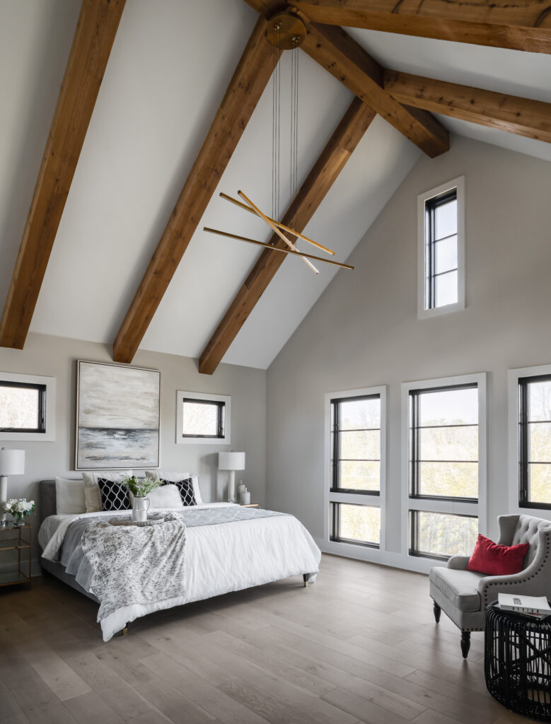 A vaulted ceiling with exposed stained beams, contemporary chandelier, and floor height windows.