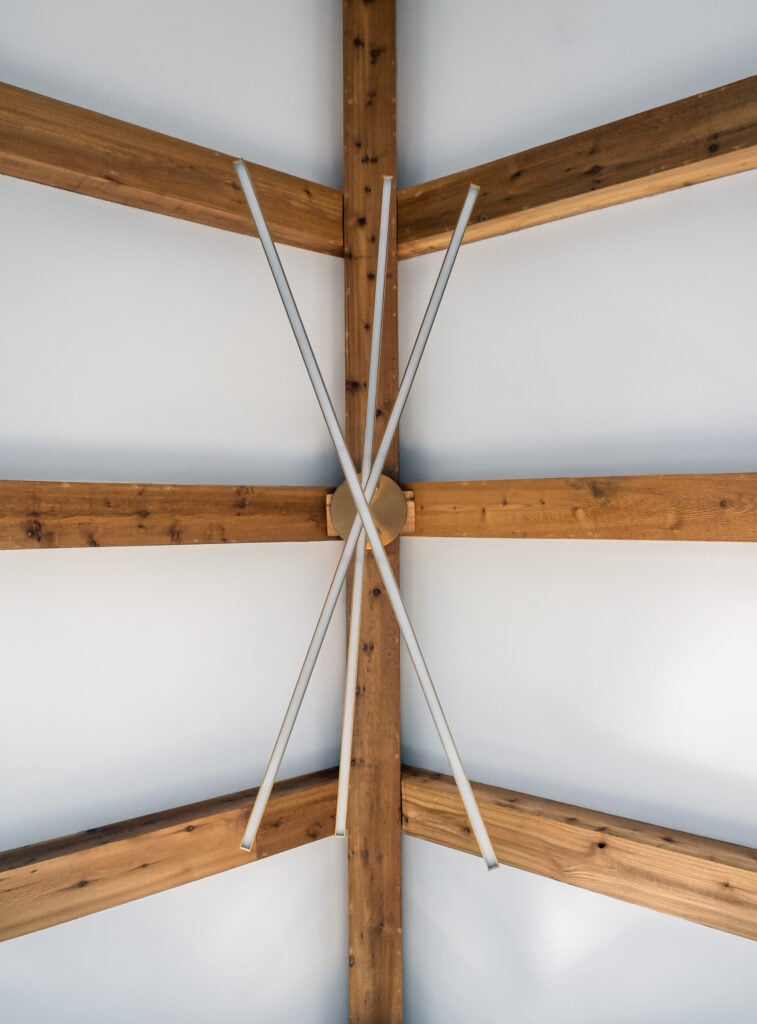 Looking upward in the Master Bedroom toward the vaulted ceiling, a geometric pattern of exposed beams with a contemporary chandelier in front.