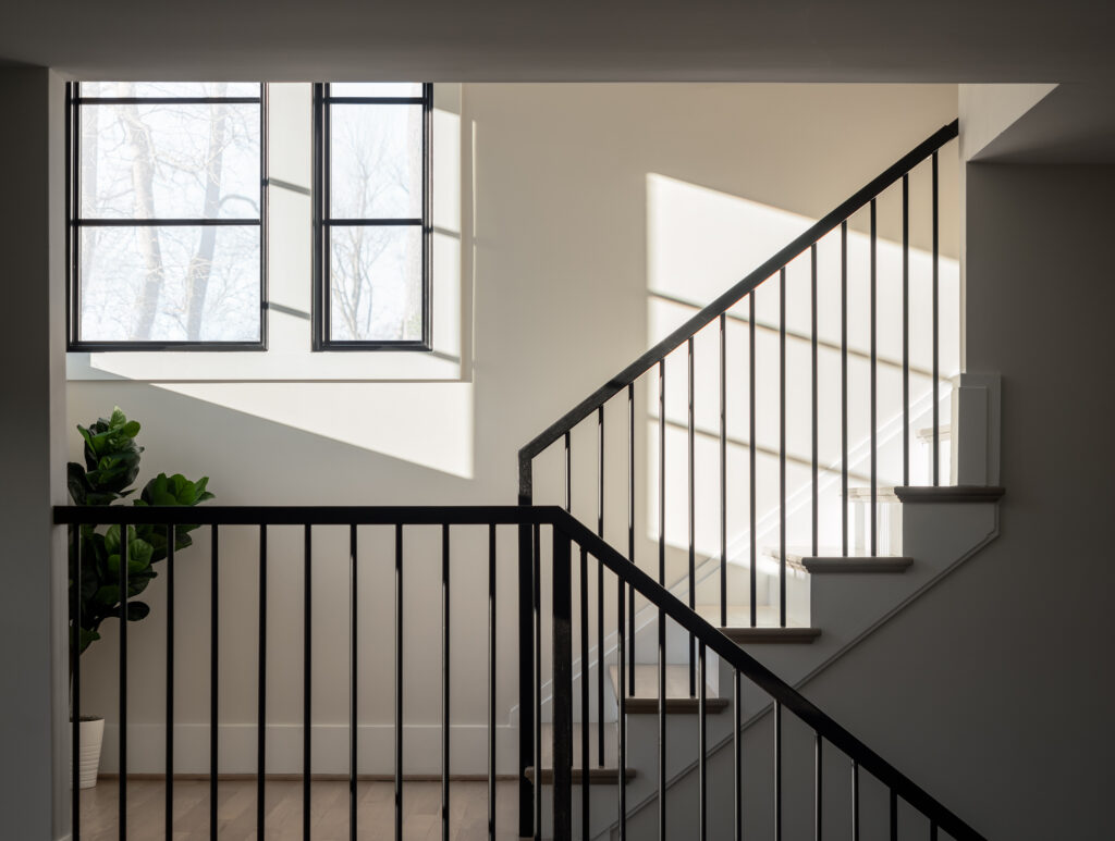 A detail photo of a sun fulled staircase, showing dark vertical iron rails and dark window frames