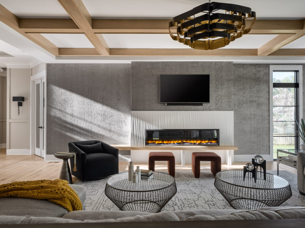 A family room with 80&rdquo; linear fireplace with custom surround of Porcelanosa&reg; Oxo Line Blanco tile, white ceiling with natural wood beam coffered ceiling.