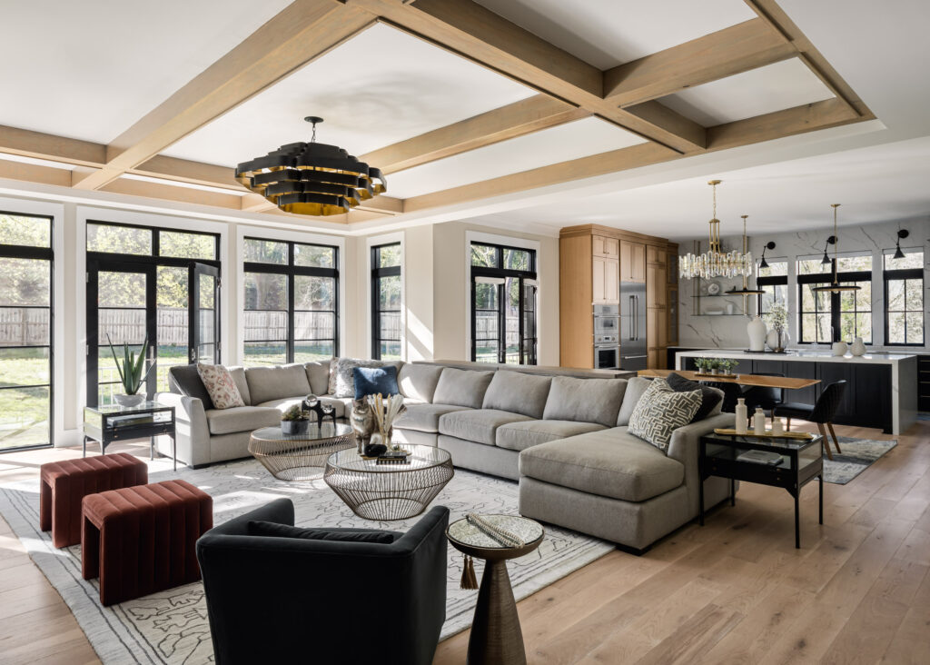 A cat stands on the table in the center of a luxury family room with large glass windows and doors to the backyard.