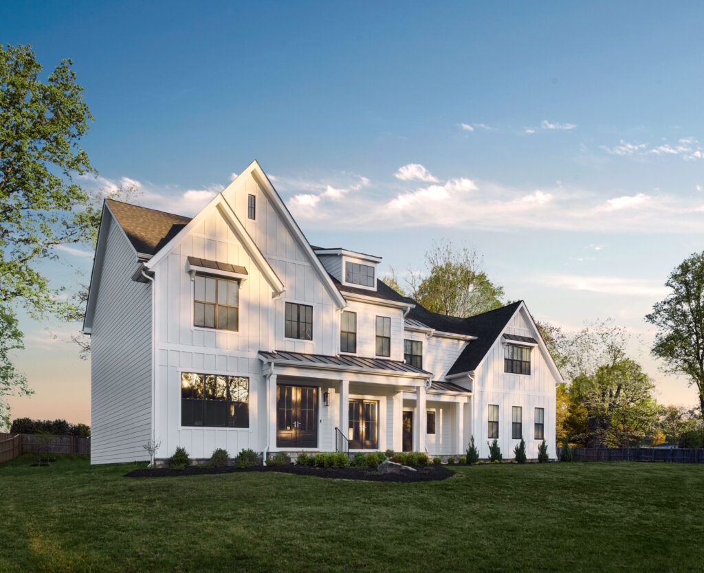 A modern farmhouse front exterior in white board and batten with two covered entrances and dark colored windows.