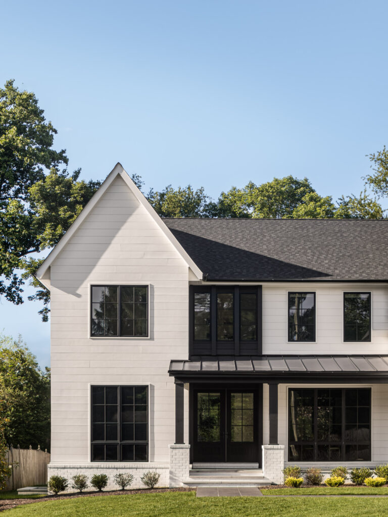 A head on photo of the left half of the front of a home in white siding with black panel accents, black windows, black porch roof, green lawn against a blue sky.