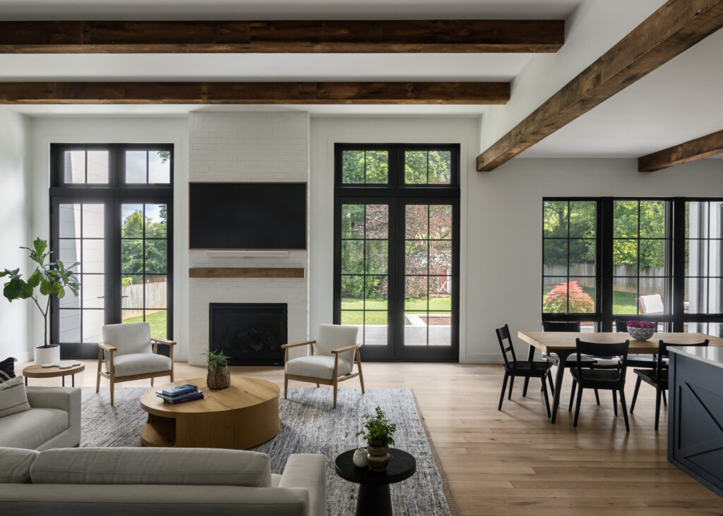 A custom modern farmhouse family room with natural exposed rough beams, two sets of doors to the patio, and kitchen island visible to the right
