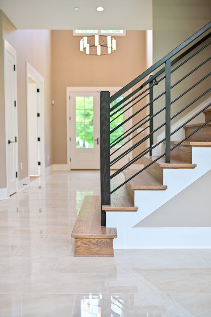 A side view of a stair case with stained wood treads and risers, darker stained posts and rails with iron horizontal rods.