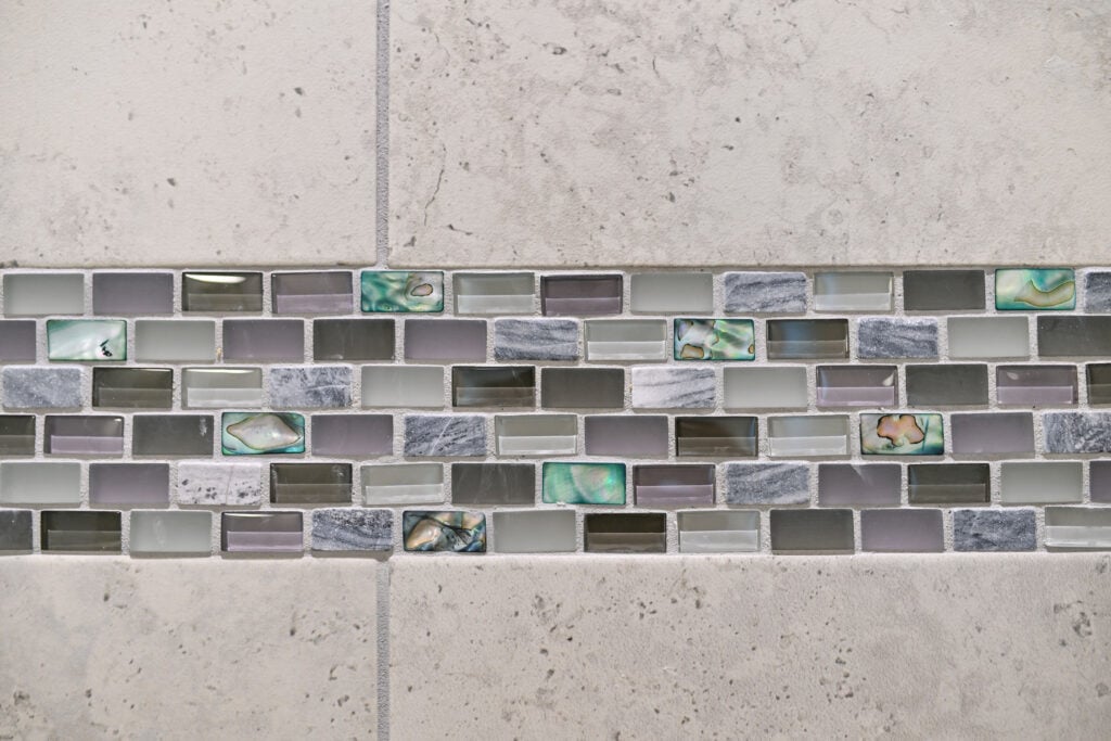 A detail image of a unique tile accent of different glass and ceramic pieces in an artful mosaic stripe.
