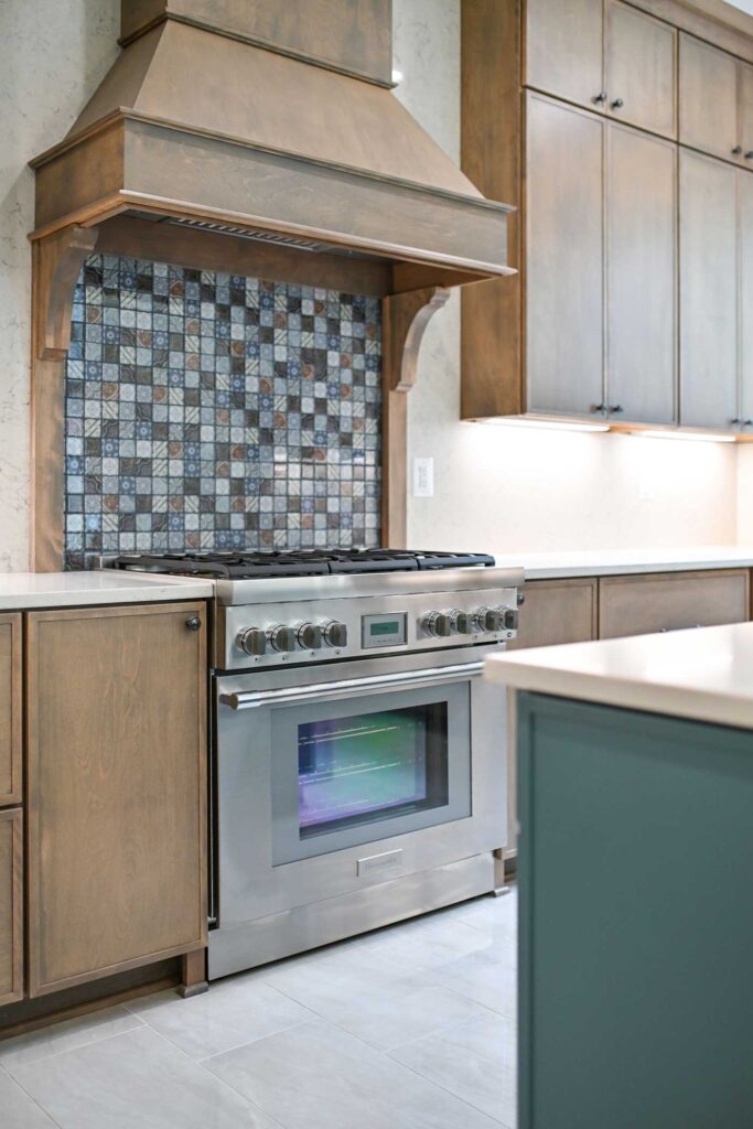 A wood encases fume hood over a commercial range and patchwork style backsplash.