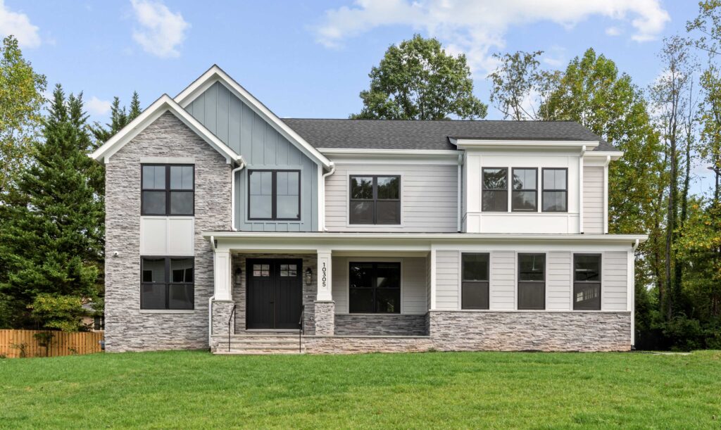 A photo look straight on at the front of a home with a mix of stacked stone, blue board and batten, grey siding and dark windows and front door