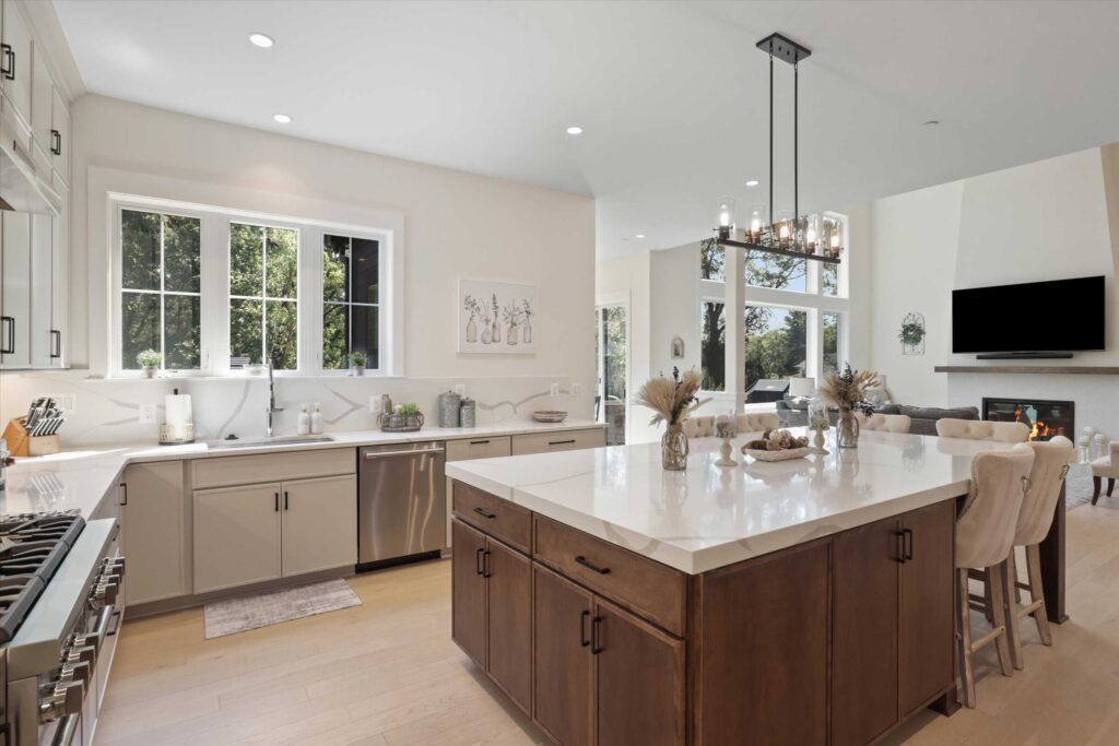 Spacious gourmet kitchen featuring a large central island with a quartz countertop and dark wood base, contrasting with light grey perimeter cabinetry and stainless steel appliances.