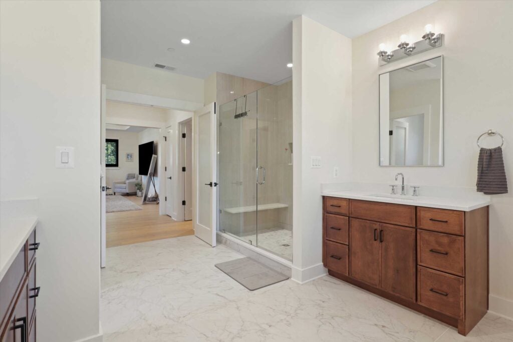 Bathroom interior showcasing a large glass-enclosed walk-in shower with a bench seat, opposite a single wood vanity with modern lighting.