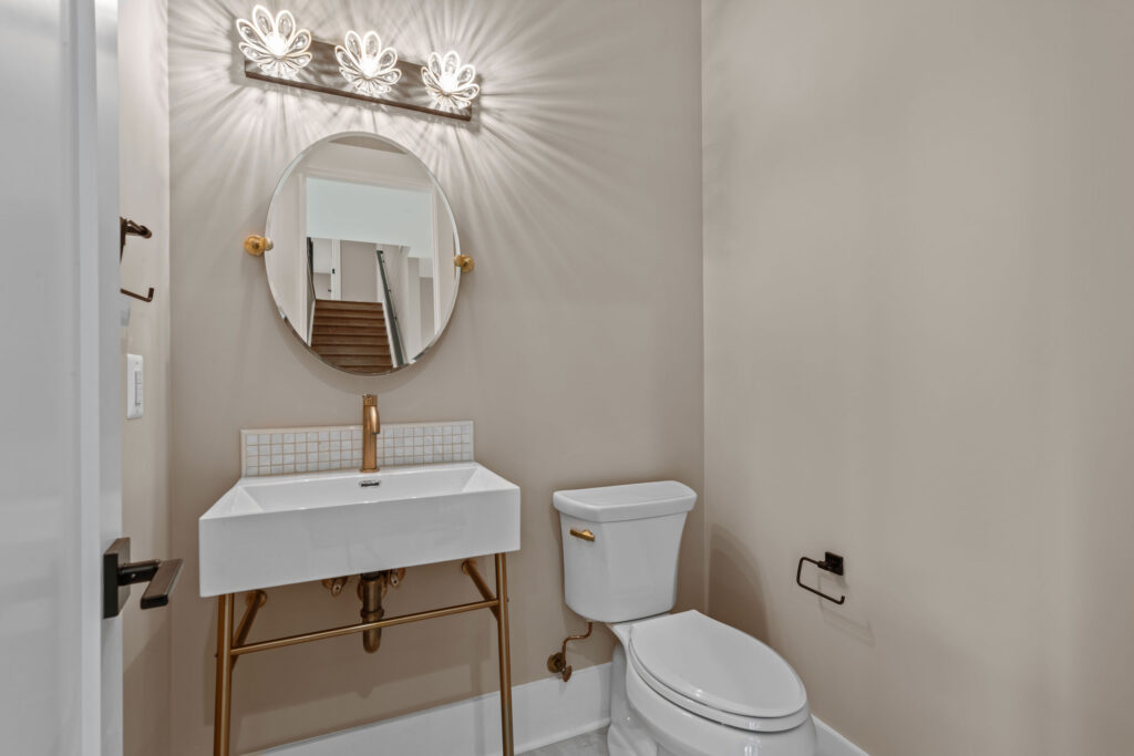 Powder room featuring a modern console sink with gold legs, a gold faucet, an oval mirror, and a decorative vanity light casting a starburst pattern.