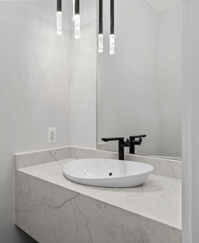 Modern powder room vanity featuring a white vessel sink sitting on a thick marble-look quartz countertop, paired with a tall black faucet.