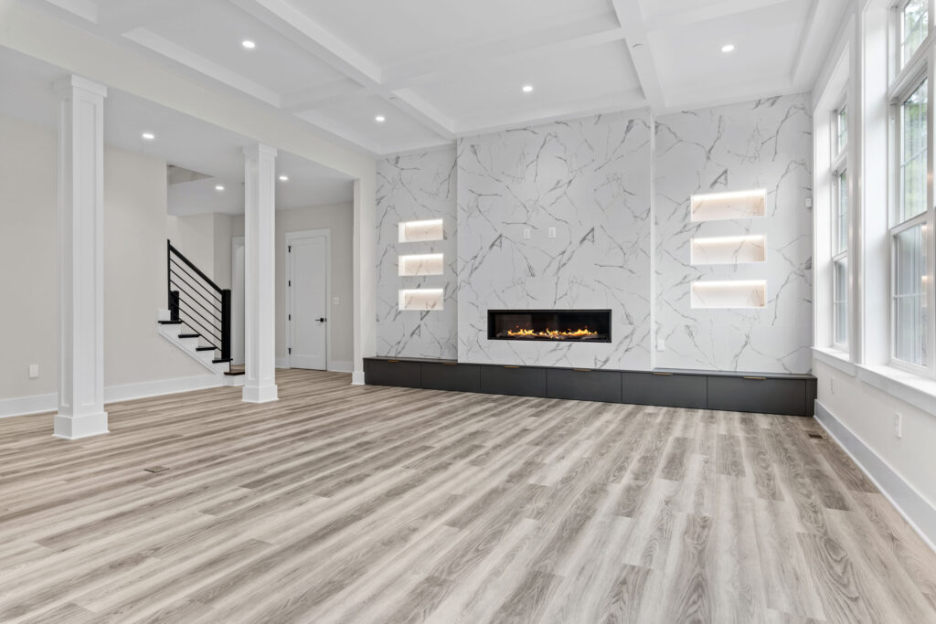 Expansive great room showcasing a coffered ceiling and a linear gas fireplace set within a massive marble-look tile wall.