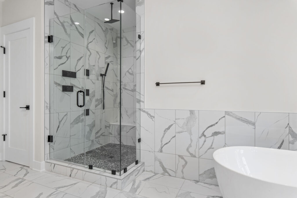 Walk-in glass shower interior featuring white marble-look tile walls, a dark pebble mosaic floor, and matte black rain shower fixtures.