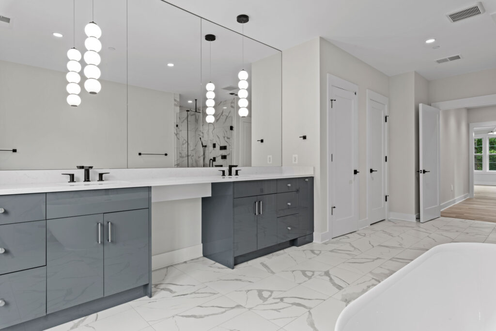 Modern bathroom featuring a long floating grey vanity with dual sinks, a large wall-to-wall mirror, and hanging sphere pendant lights.