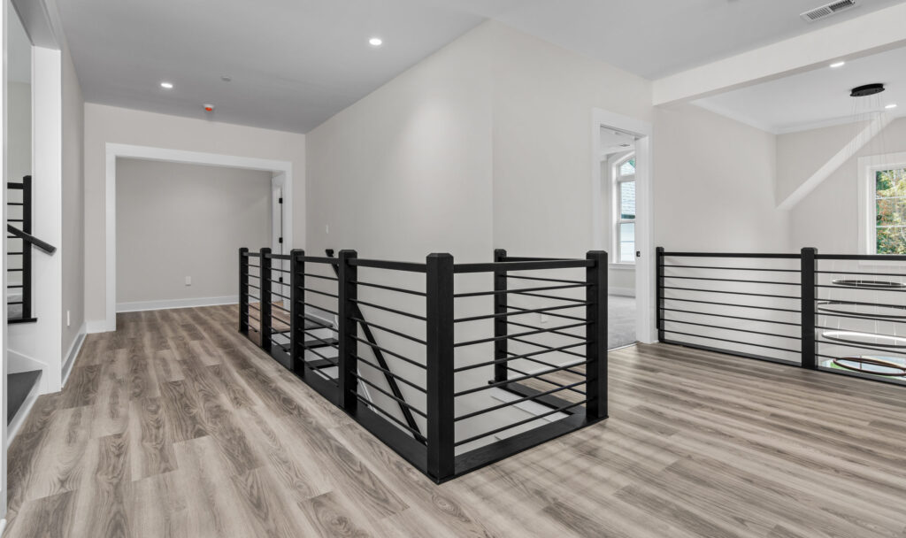 Wide upper-level hallway featuring light wood flooring, white walls, and modern black metal horizontal railings.