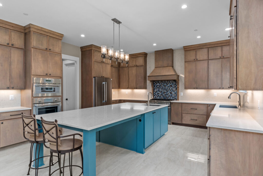 Gourmet kitchen featuring floor-to-ceiling stained wood cabinets, a large teal blue center island with white quartz countertops, and stainless steel appliances.