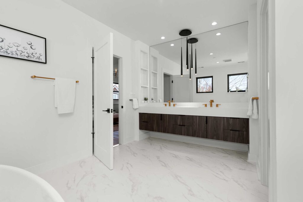 Modern primary bathroom vanity featuring dark walnut floating cabinets, white quartz countertops, gold faucets, and a cluster of sleek black tubular pendant lights reflecting in a large wall-to-wall mirror.