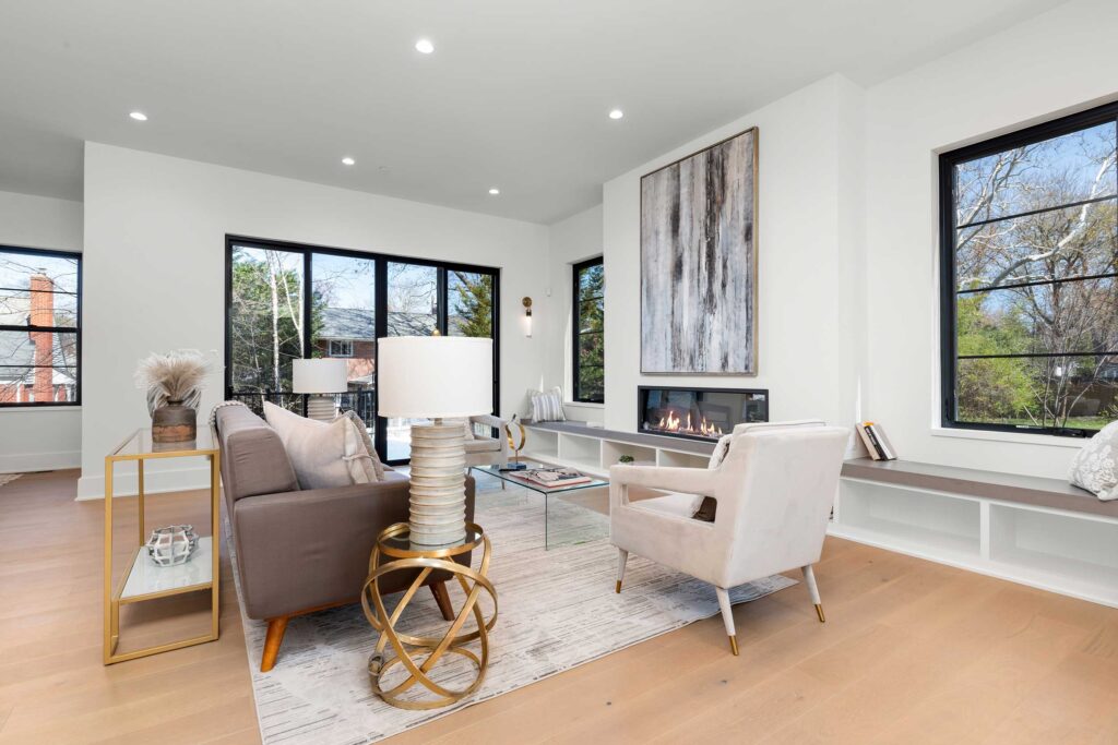 Contemporary family room with a linear gas fireplace, built-in white bench seating under large black-framed windows, and sliding glass doors leading to the outdoors.
