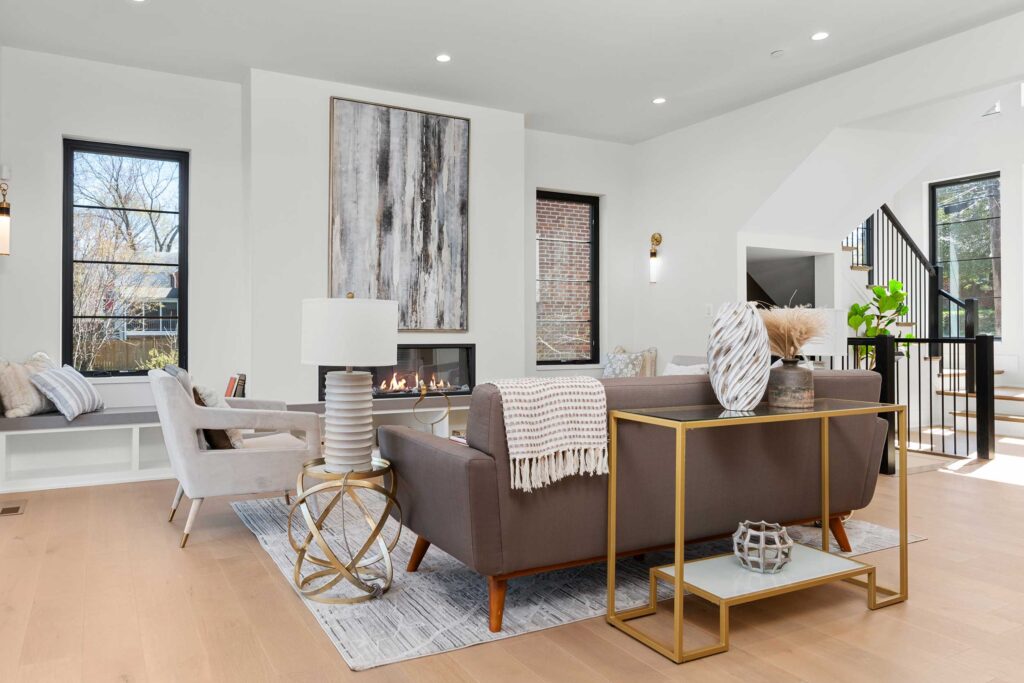 Cozy living area arrangement showing the back of a grey sofa, gold-framed console table, and a focal point fireplace with large abstract artwork above it.