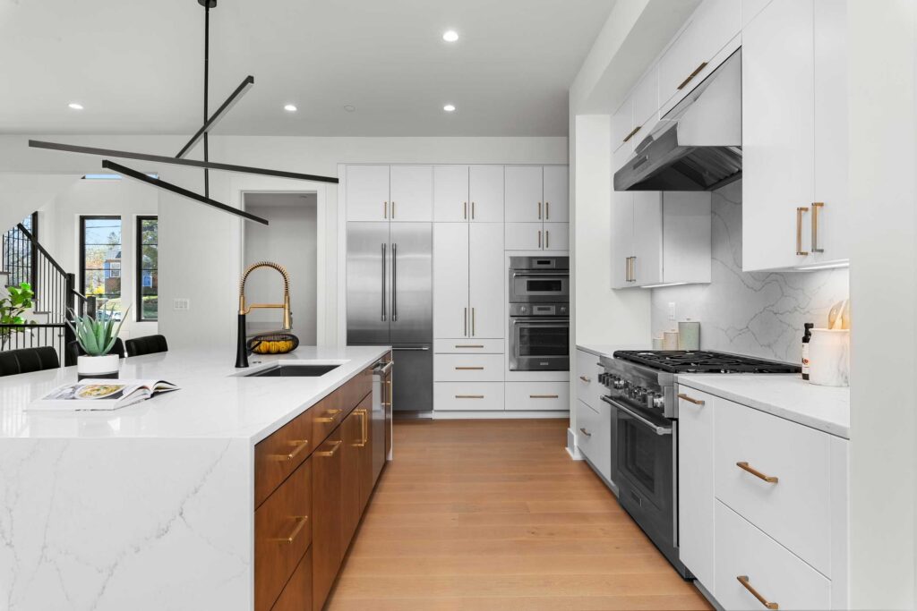 Kitchen detail shot highlighting the white quartz countertops, stainless steel gas range, double wall ovens, and custom white cabinetry with gold hardware.