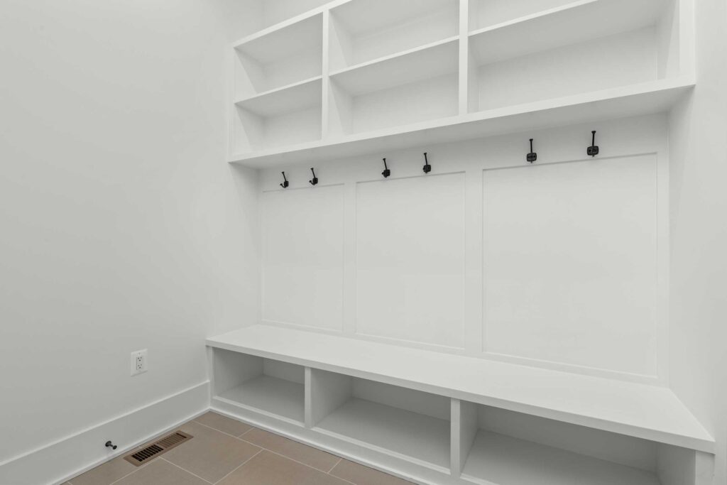 Mudroom entry area with built-in white storage cabinetry, including a bench, upper cubbies, and black coat hooks.