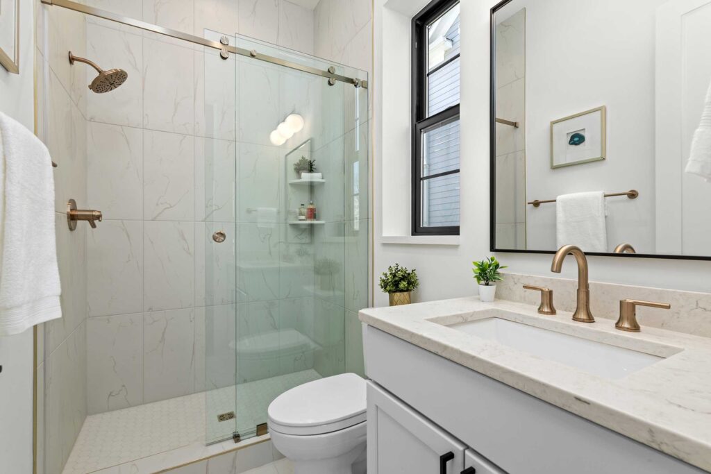 Guest bathroom featuring a white vanity with a gold faucet, a black-framed mirror, and a glass-enclosed shower with gold hardware and marble-look tile.