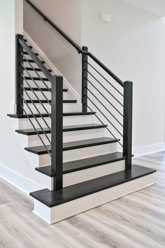 Modern staircase detail highlighting white risers, contrasting black wood treads, and sleek black horizontal metal railings.
