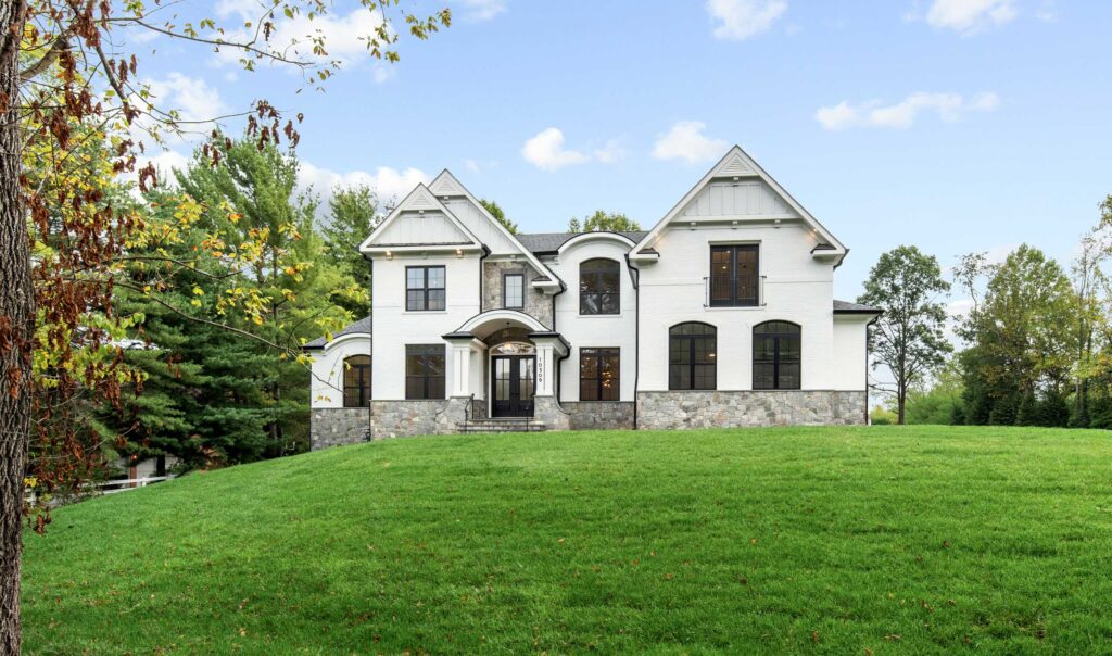 Front exterior of a luxury white brick home with dark window frames, an arched stone entry portico, and a manicured green lawn.