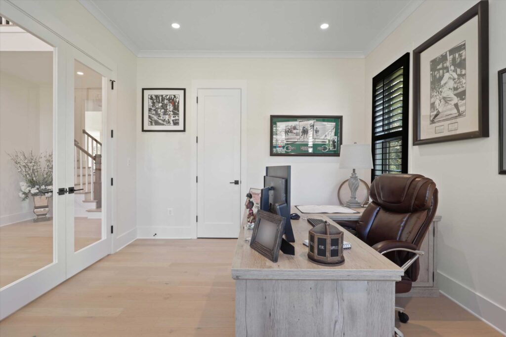 Home office space with light wood floors, a desk with a leather chair, sports memorabilia wall decor, and glass French doors.