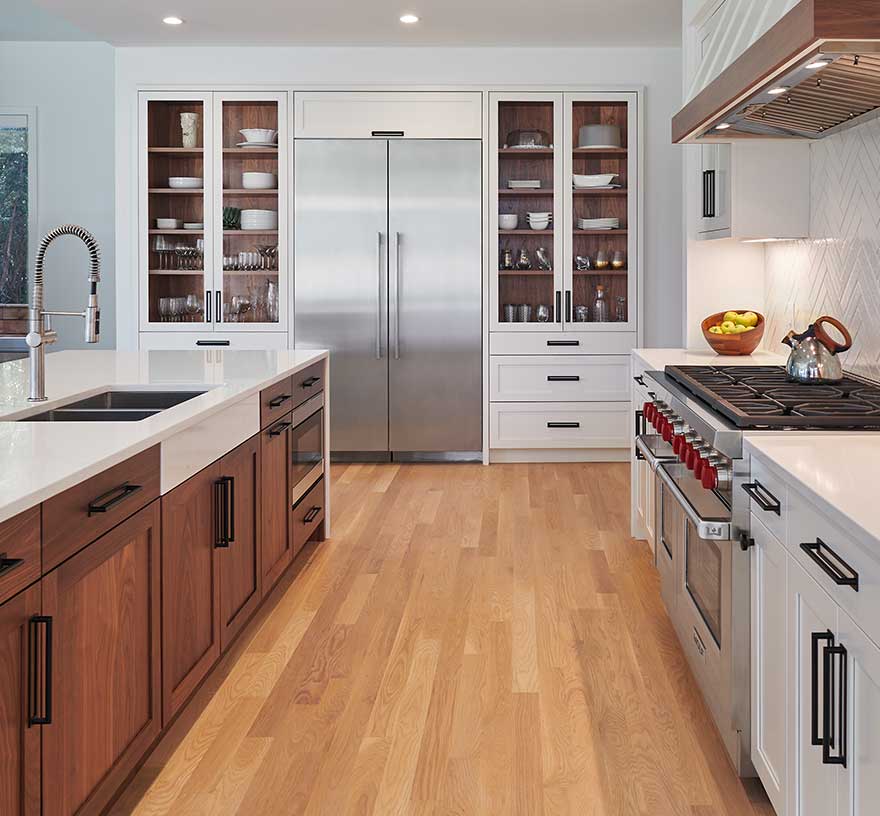 A modern kitchen with counter depth oversized refrigerator, professional range, stained wood lined cabinets with glass doors