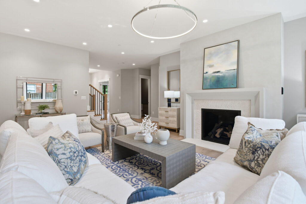 Bright living room featuring a white sectional sofa, a modern white fireplace with blue artwork, and a circular halo chandelier.