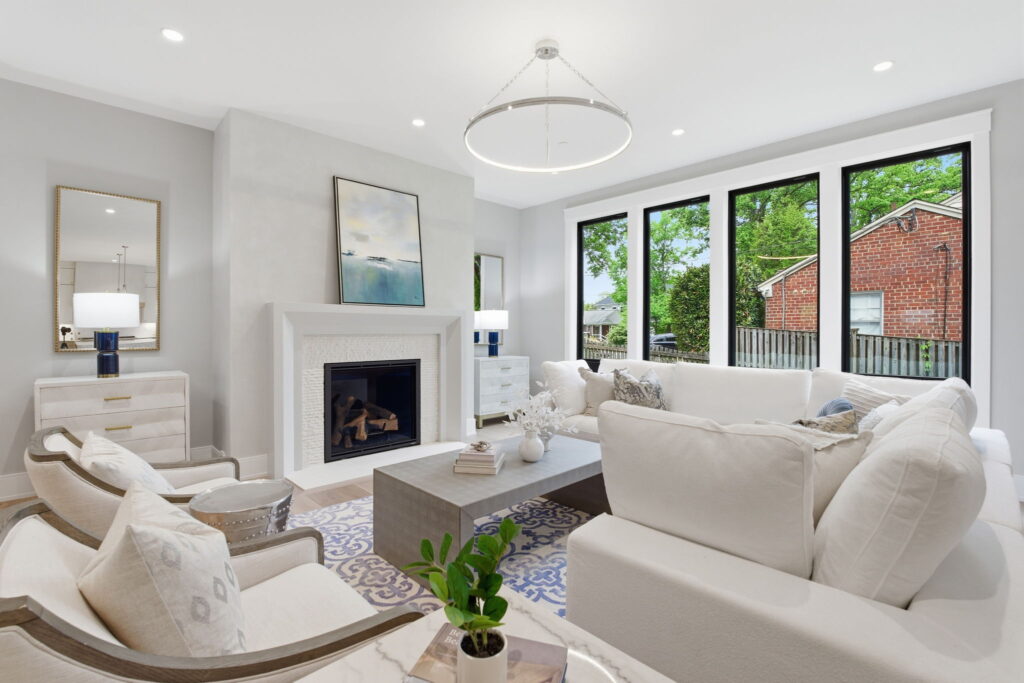 Bright living room with a white sectional sofa, two armchairs, a modern fireplace, and large windows overlooking the yard.