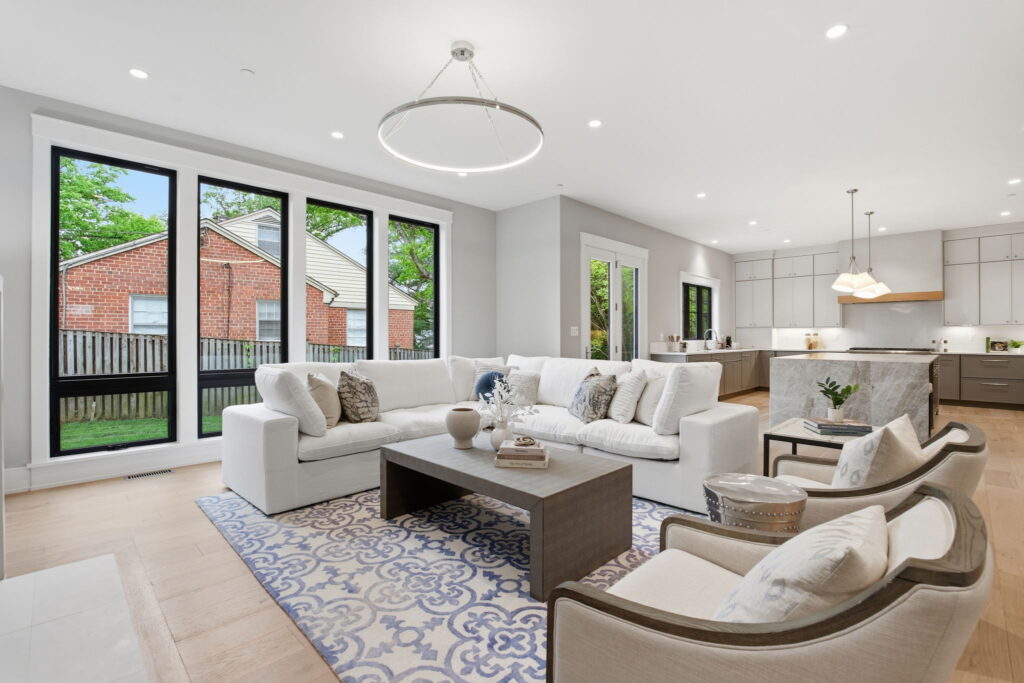 Spacious open-concept living area with a white sectional sofa, blue patterned rug, and a view into the modern kitchen with a waterfall island.