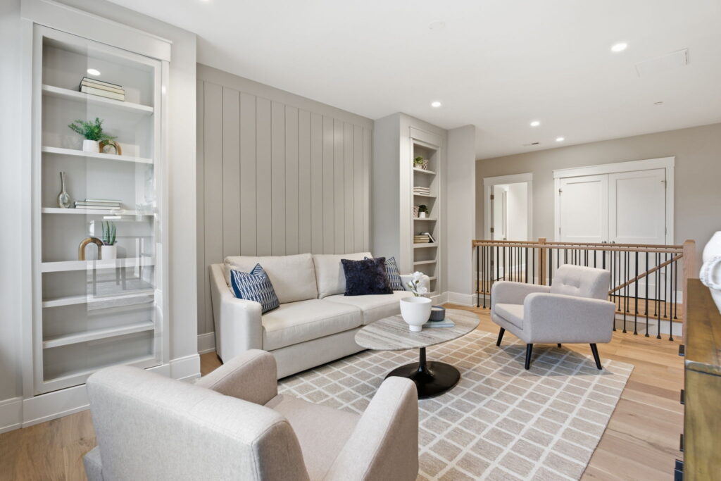 Modern upstairs loft with a cream sofa, marble coffee table, built-in bookshelves, and a light gray vertical shiplap accent wall.