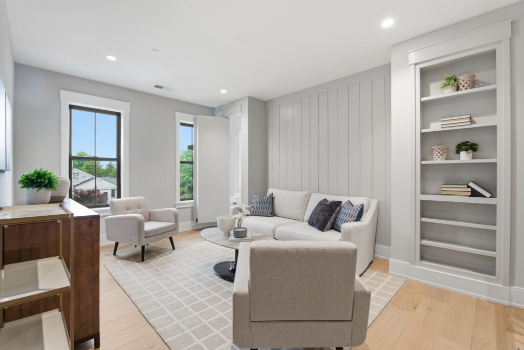 A bright upstairs loft with a white sofa, two armchairs, and a built-in bookshelf that serves as a hidden door.