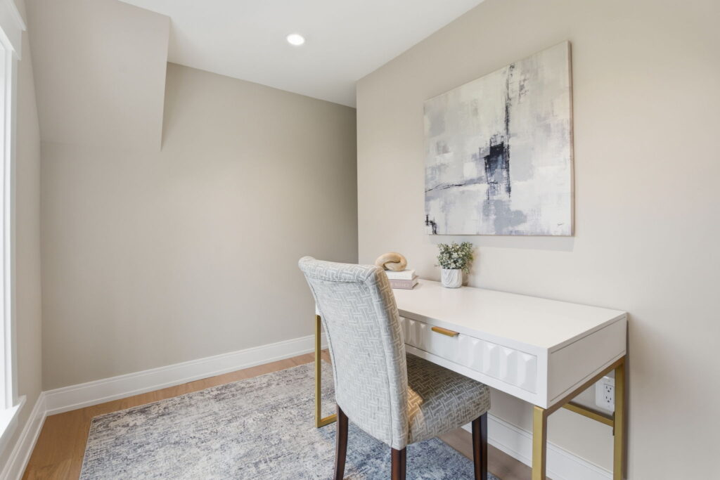 Minimalist home office with a white desk, patterned armchair, and abstract wall art in a neutral-toned room.