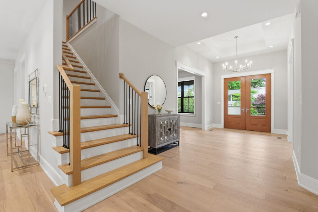 Bright home entryway featuring light wood floors, a modern wood and metal staircase, and double wooden front doors.
